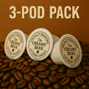 Three iFillCup-style coffee pods with The Creamy Bean logo, arranged on fresh roasted coffee beans.