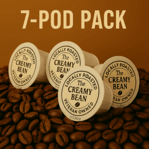Seven iFillCup-style coffee pods with The Creamy Bean logo, grouped together on a bed of fresh roasted coffee beans.